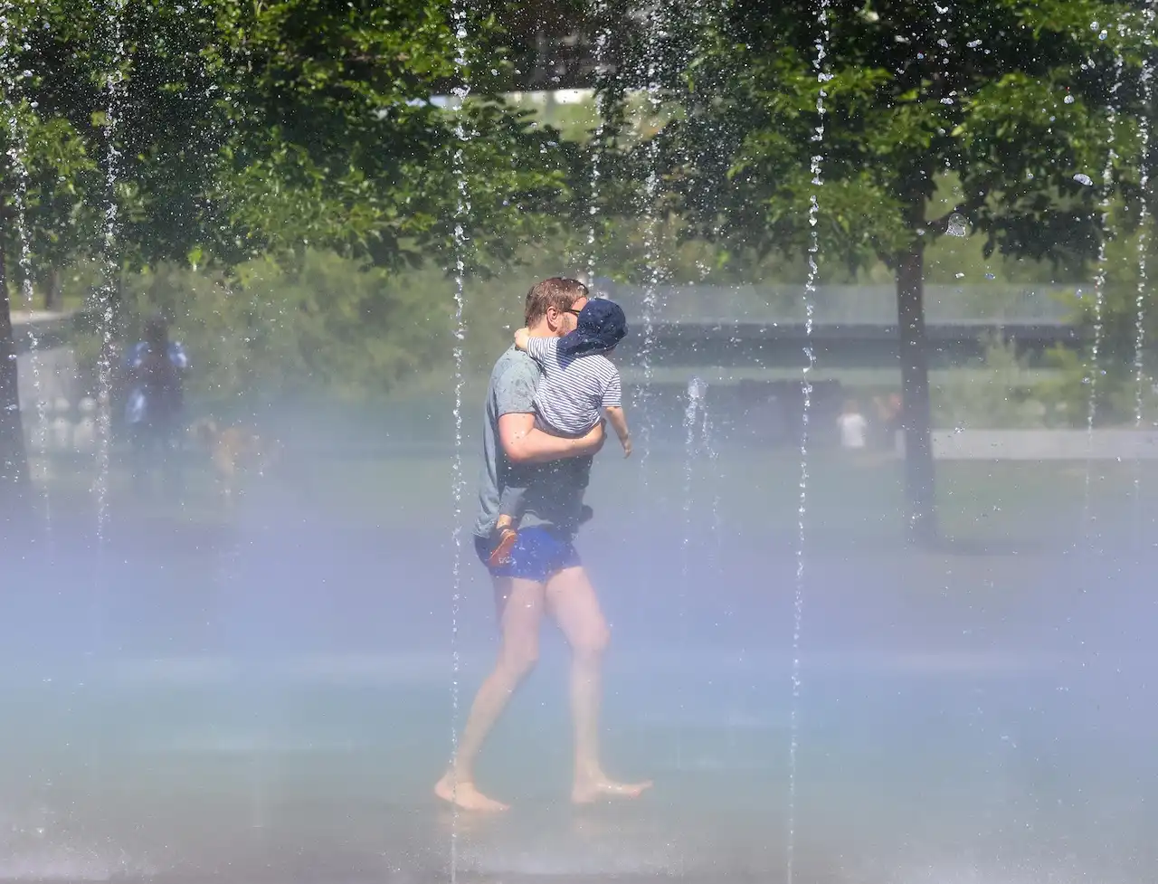 Duplica la calor en las 20 capitales más grandes del mundo. Un hombre con su hijo pasa por los chorros de agua de la playa de Madrid Río / Foto: EP